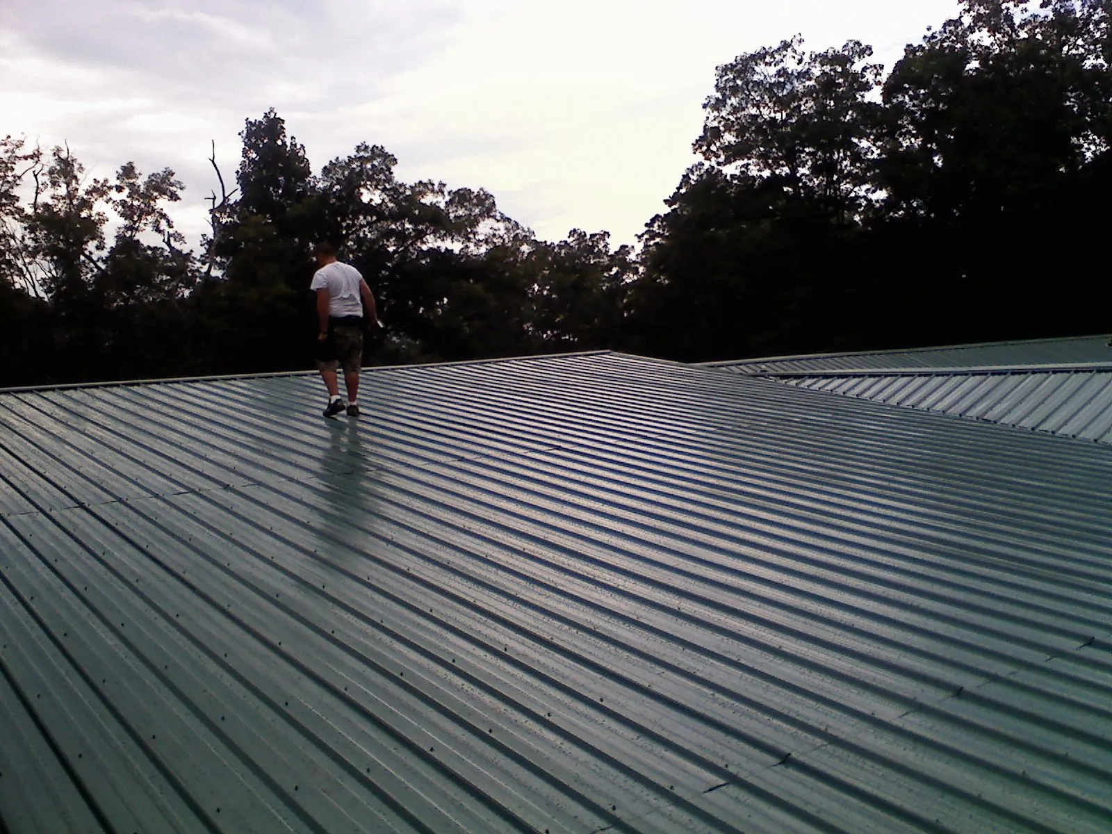 Roofer walking a wide expanse of new green metal roofing in Wilmington